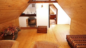 A cozy attic room with a fireplace, wooden beams, and a view into a kitchen.