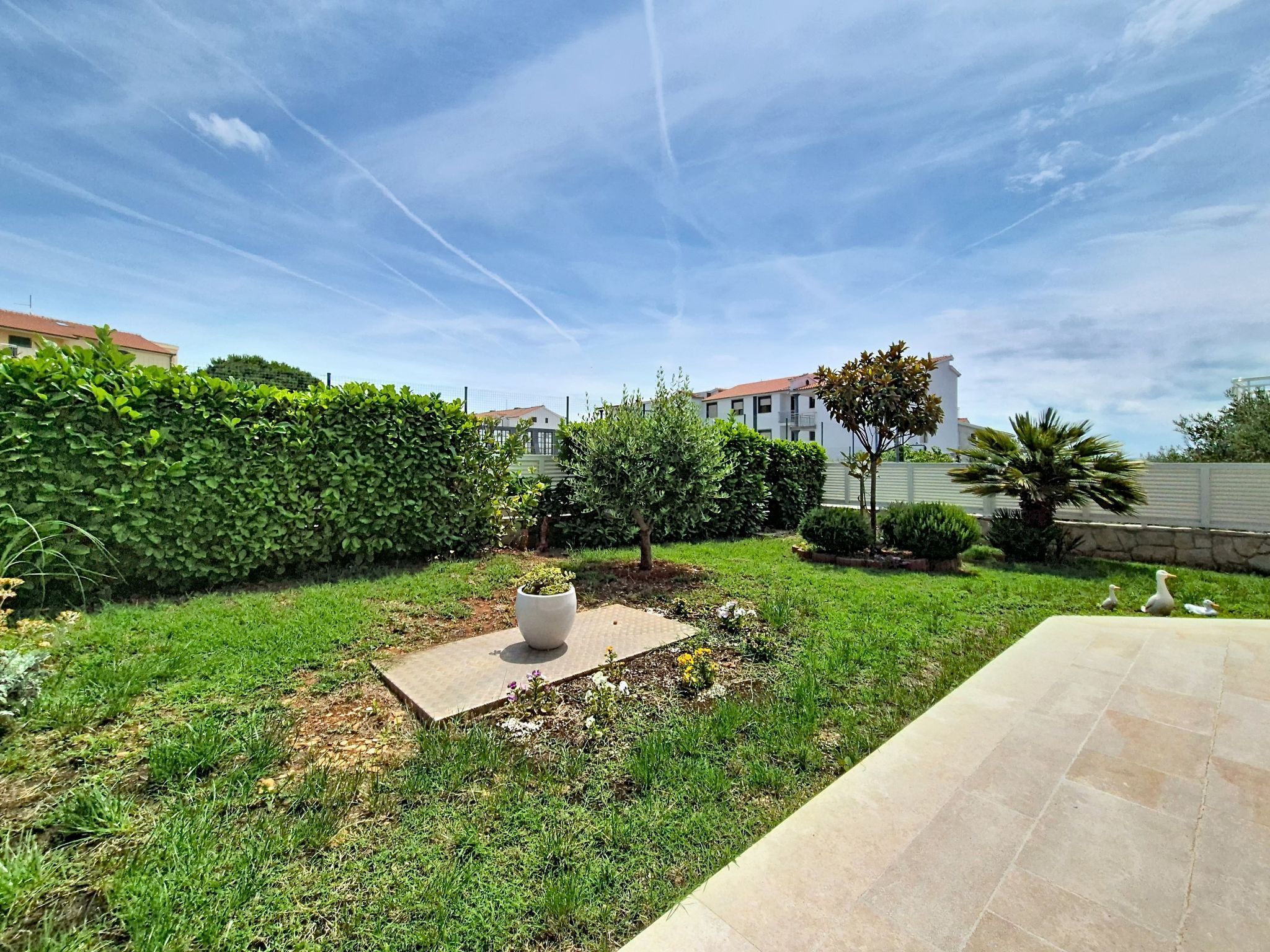 A well-maintained garden with a paved patio area, neatly trimmed hedges, and a variety of plants.