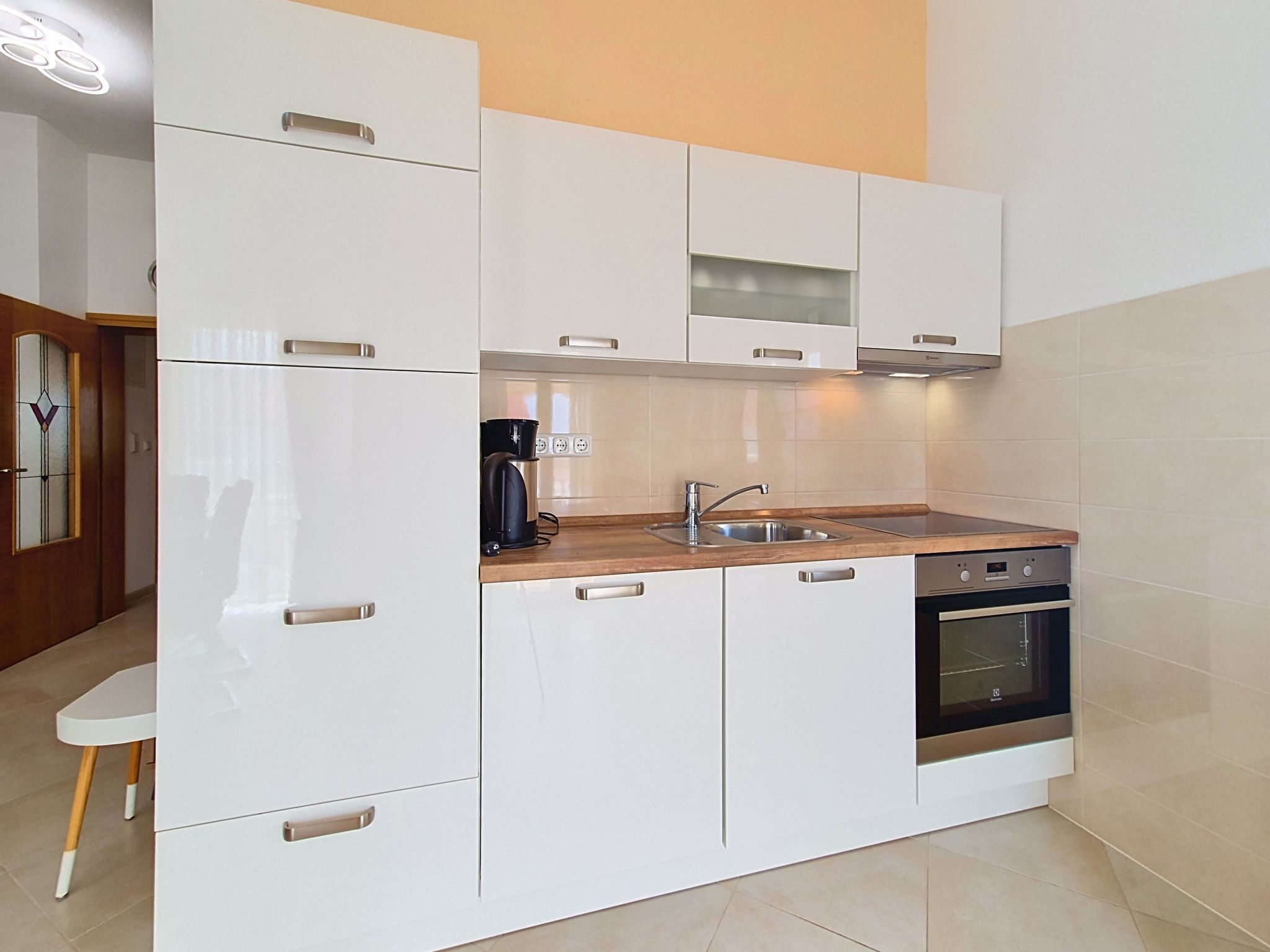 A modern kitchen with white cabinets, a wooden countertop, a built-in oven, and a stainless steel sink.