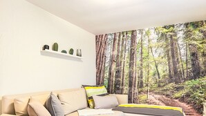 En stue med en beige sofa, et hvidt sofabord og et tapet med skovmotiv.