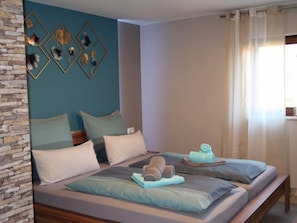 A bedroom with a stone wall, a bed with multiple pillows, a bedside table, and a window with curtains.