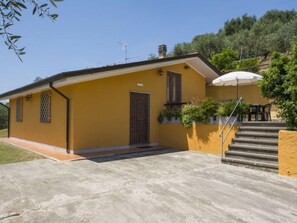 Edifici groc amb un pati de formigó, una escala i una petita zona de seients a l'exterior.