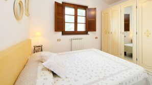 Une chambre à coucher avec un lit, une fenêtre avec des volets en bois, un radiateur et une armoire.