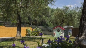 Un jardin agrémenté d’une petite nichée à oiseaux blanche et verte, entouré de fleurs et d’arbres aux couleurs violettes.