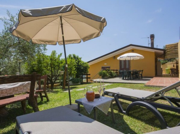 Zona de pati amb mobiliari exterior, incloent una taula i caires, i un parasol gran que ofereix ombra.