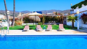 Ein Poolbereich mit Liegestühlen, einer Hängematte und einer Pergola mit einem Reetdach.