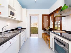 Una cocina moderna con armarios blancos, encimera negra, horno empotrado y ventana con vistas a zonas verdes.