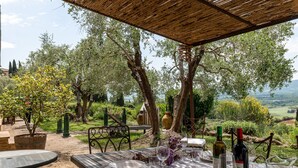 Un espace de restauration en plein air avec une table dressée pour deux personnes, entouré d’oliviers et offrant une vue pittoresque.