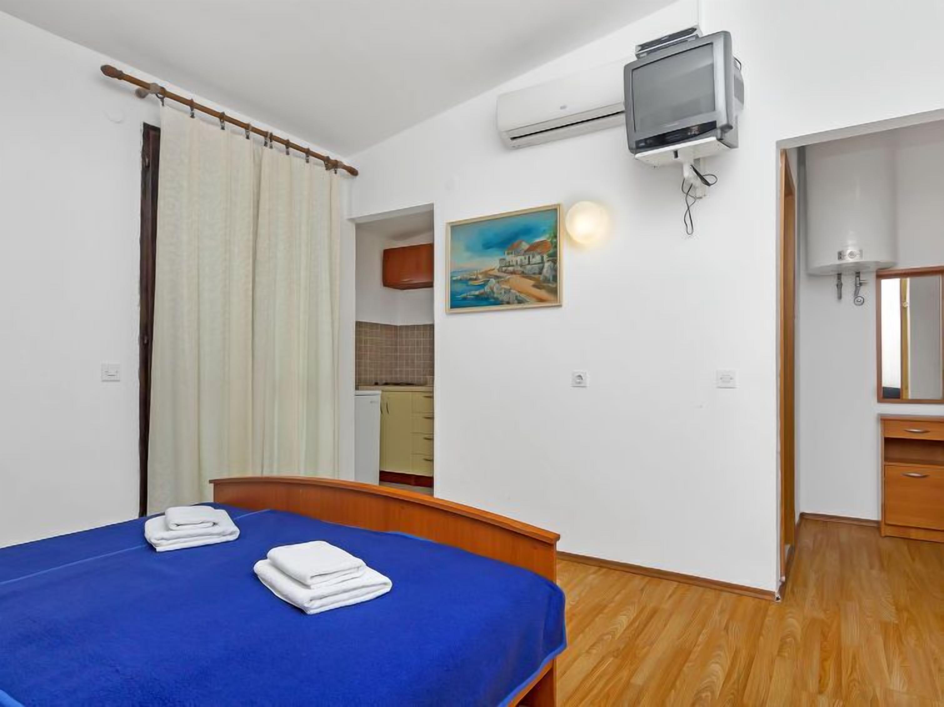 A bedroom with a bed, a painting, an air conditioning unit, and a bathroom visible through an open door.