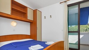 Ett hotellrum med en säng, ett träbeklätt sänggavel, en inbyggd hylla, en väggmonterad lampa och en skjutdörr i glas som leder ut till ett utomhusområde.