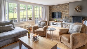 A cozy living room with a stone wall, a fireplace, and a large window overlooking a garden.