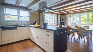 A modern kitchen with wooden beams, a central island, and a dining area with natural light.