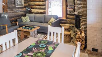 Een gezellig blokhutinterieur met een bank, stoelen, een tafel met een decoratieve tafelkleed, een open haard en een raam met gordijnen.