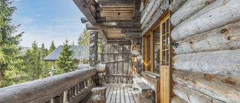 A wooden log cabin with a wooden deck and a glass door leading to a covered porch.