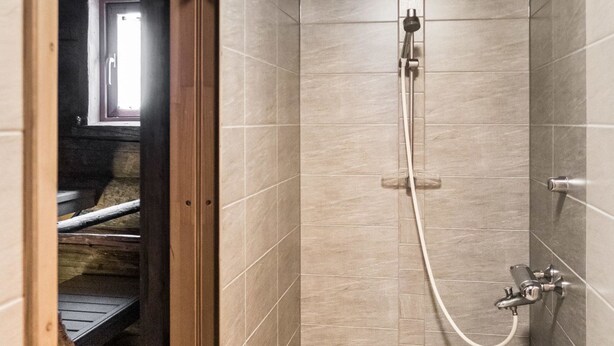 Une salle de bain avec des carreaux de couleur beige, une douche équipée d’un pommeau de douche amovible et une poignée de porte visible.