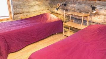 Een slaapkamer in een blokhut met twee bedden, houten vloeren en een plankunit.