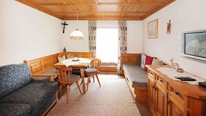 A cozy room with a wooden ceiling, a dining table with chairs, a bench, a sofa, and a cabinet with a television.