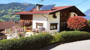 A house with solar panels on the roof, a garden with flowers, and a mountain view in the background.