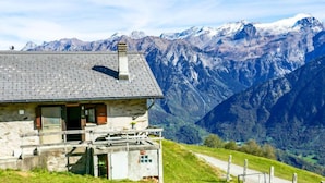 A stone house with a sloped roof, a chimney, and a balcony overlooking a mountainous landscape. - Baita Ficc by Interhome (Ponto Valentino)