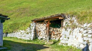 A stone wall with a small wooden structure, possibly a shed, and a pile of firewood. - Baita Ficc by Interhome (Ponto Valentino)
