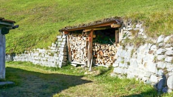Un muro di pietra con una piccola struttura in legno, forse un deposito, e una pila di legna da ardere.