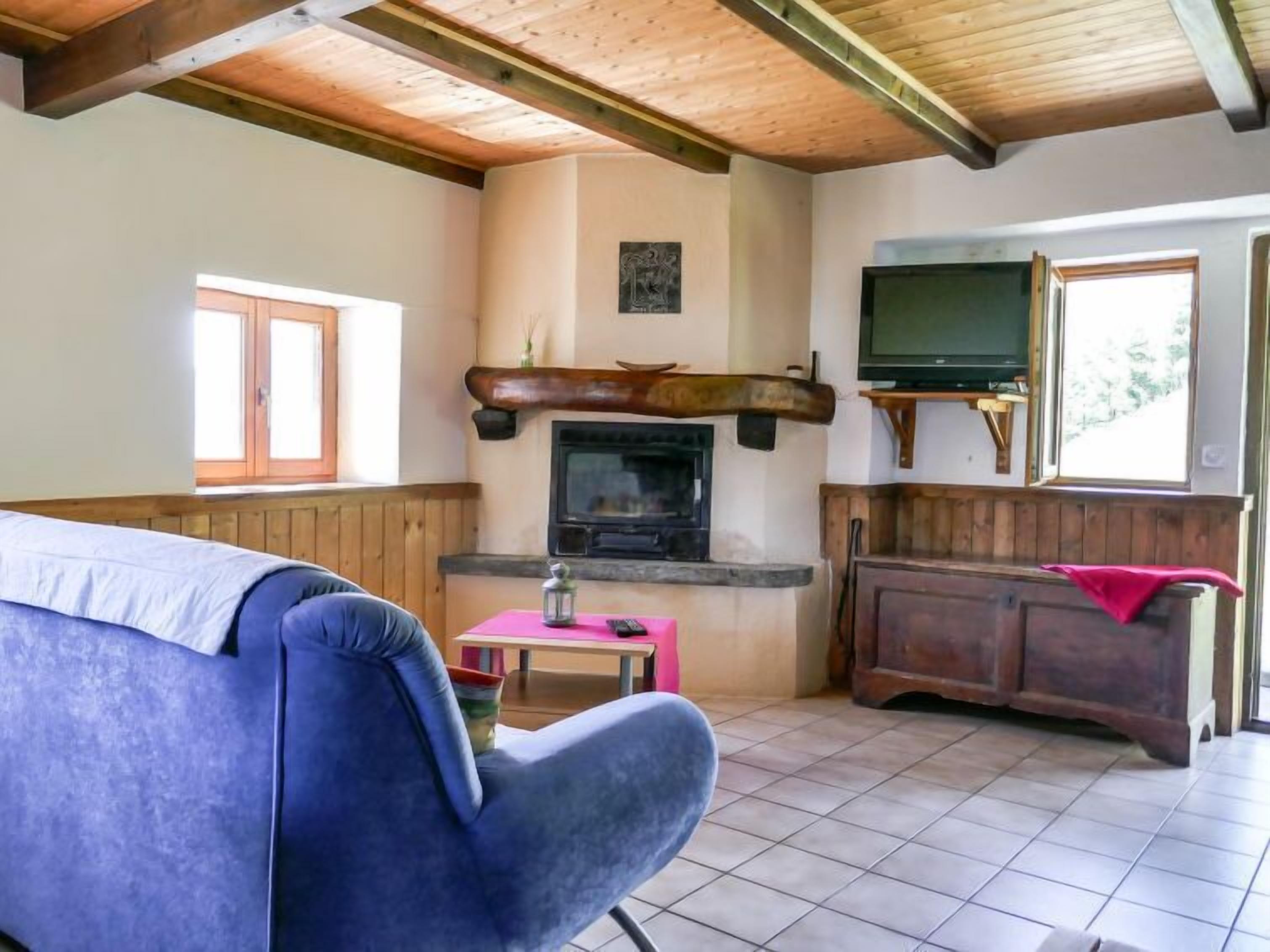 Ein gemütliches Wohnzimmer mit einem blauen Sofa, einem Kamin, einem Fernseher und Holzbalken an der Decke.