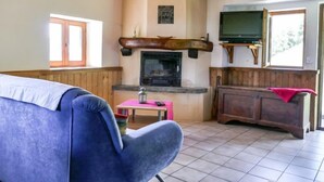 A cozy living room with a blue sofa, a fireplace, a television, and wooden beams on the ceiling. - Baita Ficc by Interhome (Ponto Valentino)
