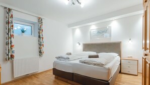 Une chambre moderne avec un grand lit, une fenêtre ornée de rideaux à motifs floraux, un radiateur, un luminaire au plafond et une table de chevet avec une lampe.