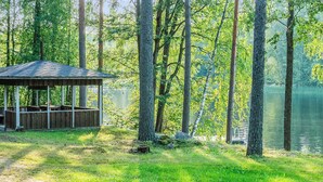 En trälusthus vid en sjö, omgiven av höga träd.