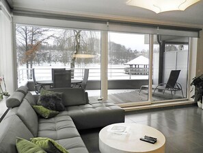 Ein modernes Wohnzimmer mit Ecksofa, rundem Couchtisch und einer großen Schiebeglastür, die auf einen Balkon mit Sitzgelegenheit führt.