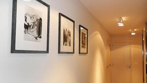 Un couloir avec trois photographies encadrées accrochées au mur, une porte au fond et un éclairage encastré.