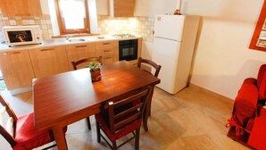 Cozinha compacta com armários de madeira, geladeira branca, micro-ondas e mesa de jantar com cadeiras.
