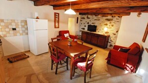 Um quarto acolhedor com uma mesa de jantar de madeira, cadeiras vermelhas, uma parede de pedra, uma televisão e um frigorífico branco.