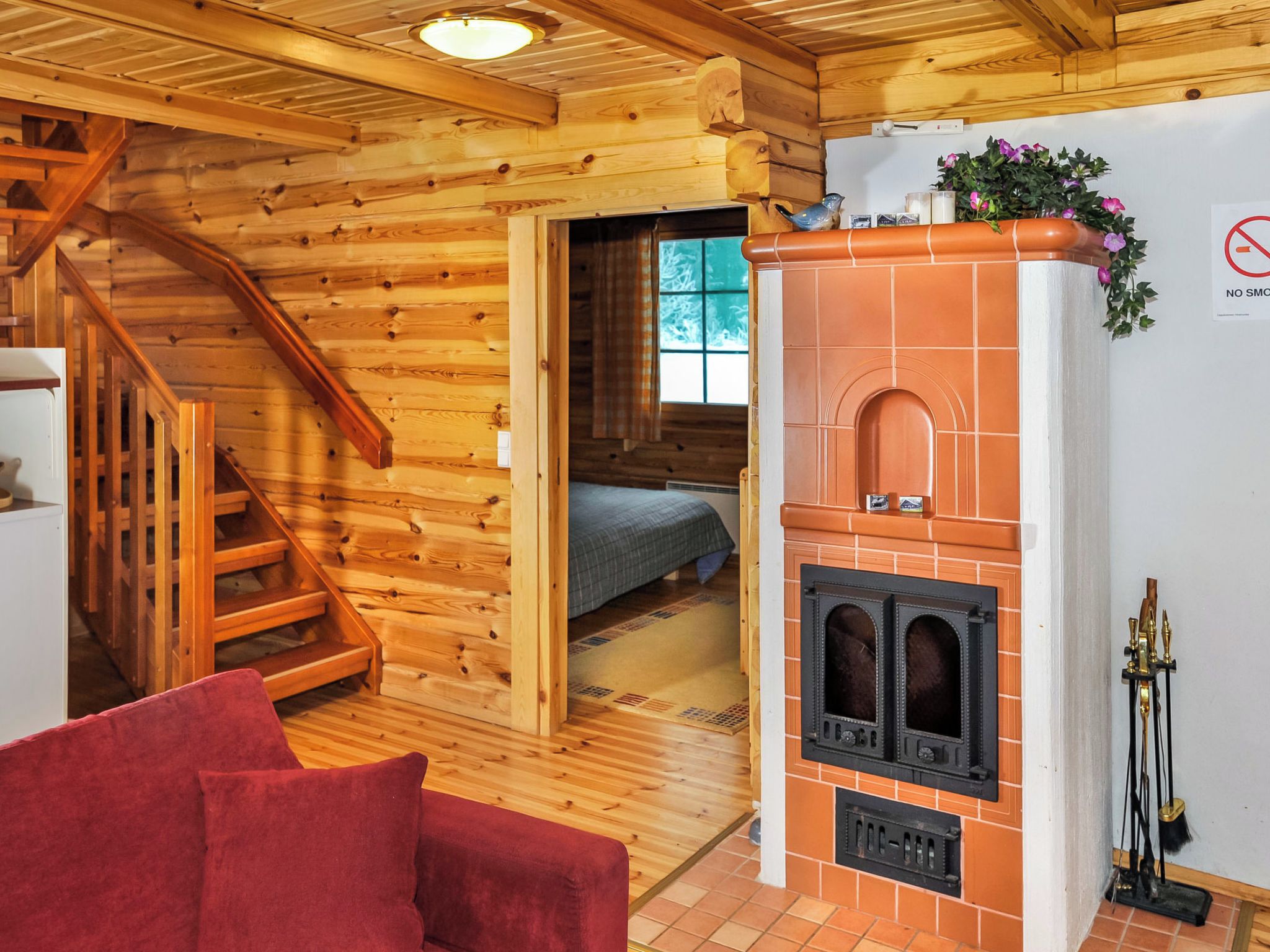 A wooden cabin interior with a fireplace, a bed, and a red sofa.