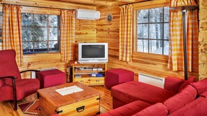 Un accogliente interno di una baita con pareti in legno, televisore, arredamento rosso e ampie finestre con tende.