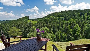 Una terraza de madera con una mesa y sillas que da a una ladera boscosa.