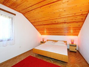 Une chambre avec un plafond en pente, un plancher en bois, un lit recouvert d’un tapis rouge et des lampes de chevet.