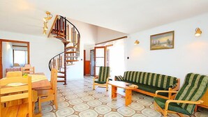 Amplia sala de estar con una mesa de comedor de madera, sillas, un sofá verde a rayas y una escalera en espiral.