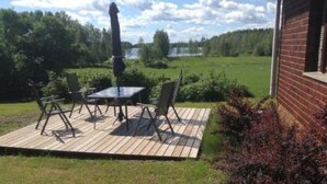 Um pátio externo com mesa e cadeiras, rodeado por um deck de madeira e uma parede de tijolos.