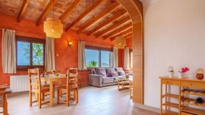 A spacious room with a wooden ceiling, a dining area with a table and chairs, a sofa, and a wooden cabinet with shelves. - Cala Torta Na Moli by Interhome (Cala Torta)