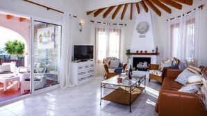 Amplia sala de estar con chimenea, televisor y puerta de vidrio que da a un espacio al aire libre.