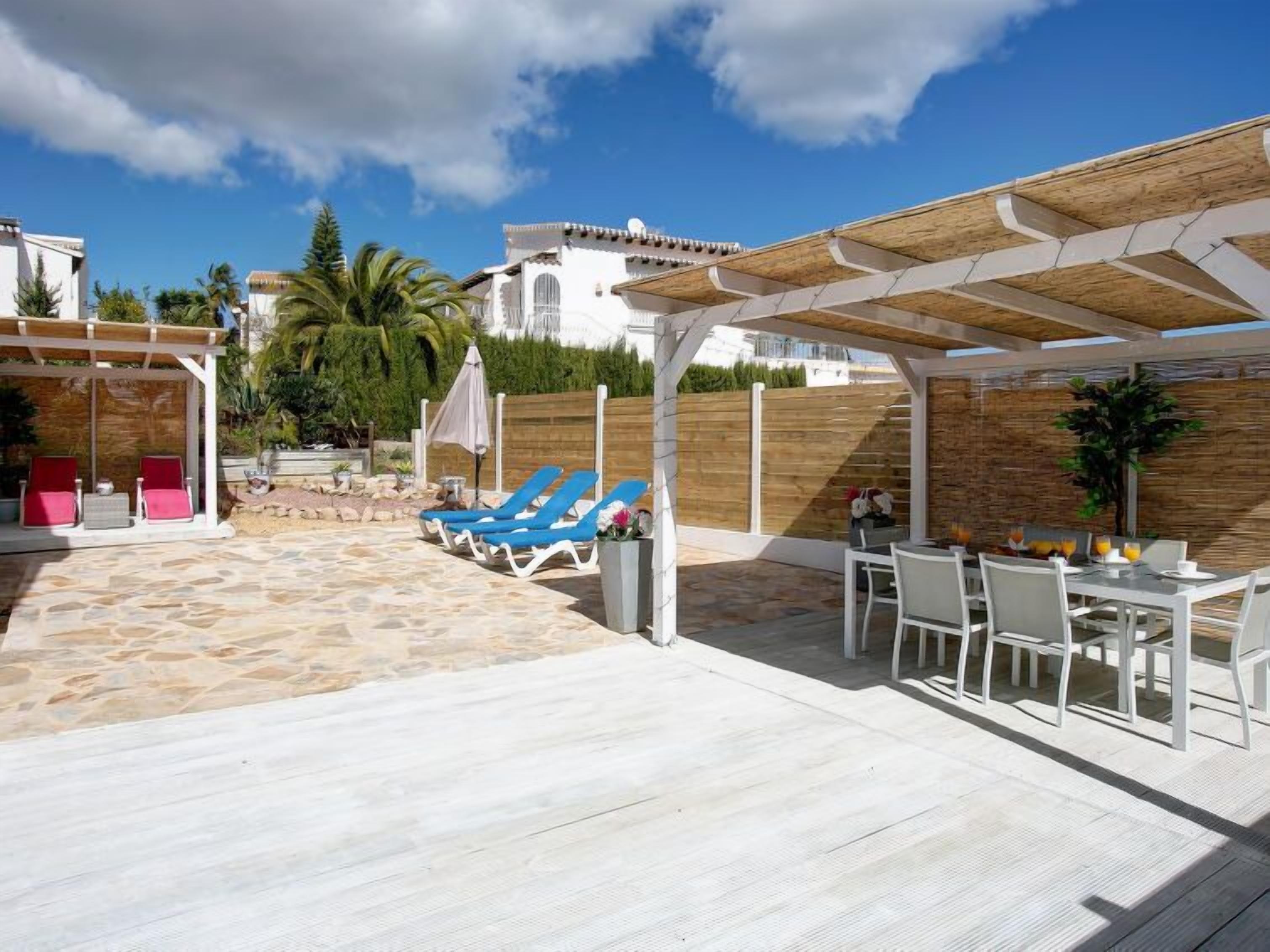 A covered outdoor area with stone flooring, blue lounge chairs, and a table with chairs.