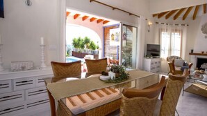Comedor con mesa de vidrio, sillas de mimbre y vistas a una piscina y zona exterior.