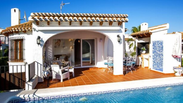 Una villa con piscina, mobiliario de exterior y un patio cubierto.