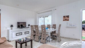 A modern living room with a sofa, a dining table with chairs, a TV, and a kitchen area with cabinets. - Mercury by Interhome (Lloret de Mar)