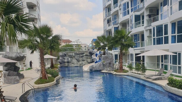 Ein Swimmingpool mit Rutsche, umgeben von Palmen und modernen Gebäuden.