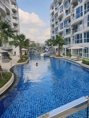 Una piscina con tobogán, rodeada de palmeras y edificios modernos.