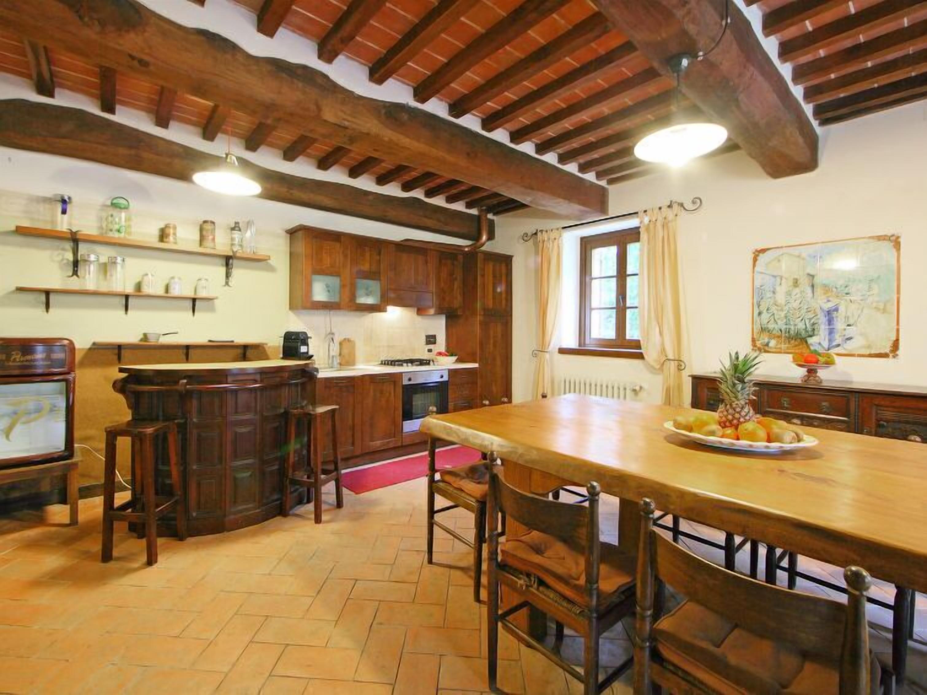A rustic kitchen with wooden beams, a large dining table, and bar stools.