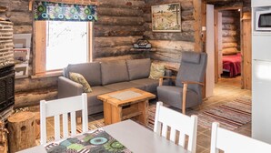 A cozy log cabin interior with a sofa, armchairs, a dining table, and a kitchen area. - Rukajoiku 1 by Interhome (Kuusamo)