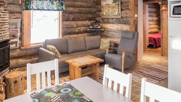 A cozy log cabin interior with a sofa, chairs, a table, and a kitchen area.